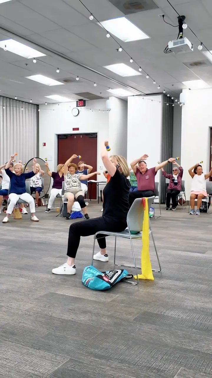 An instructor leading a seated Dance for Wellness session with resistance bands